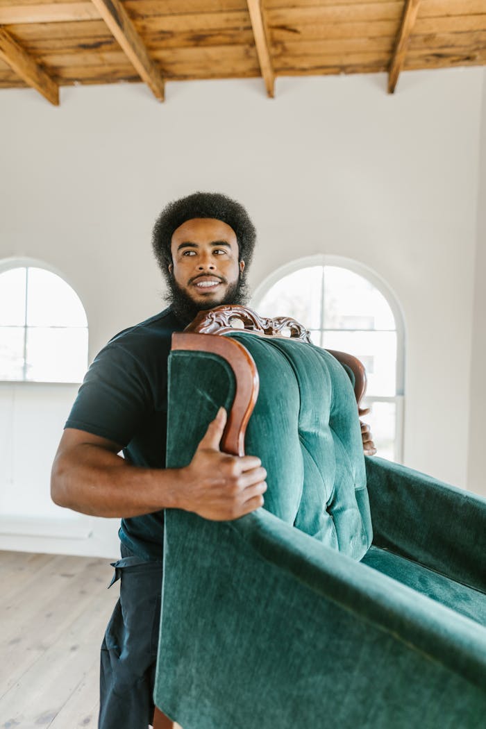 Man Smiling While Lifting a Green Armchair